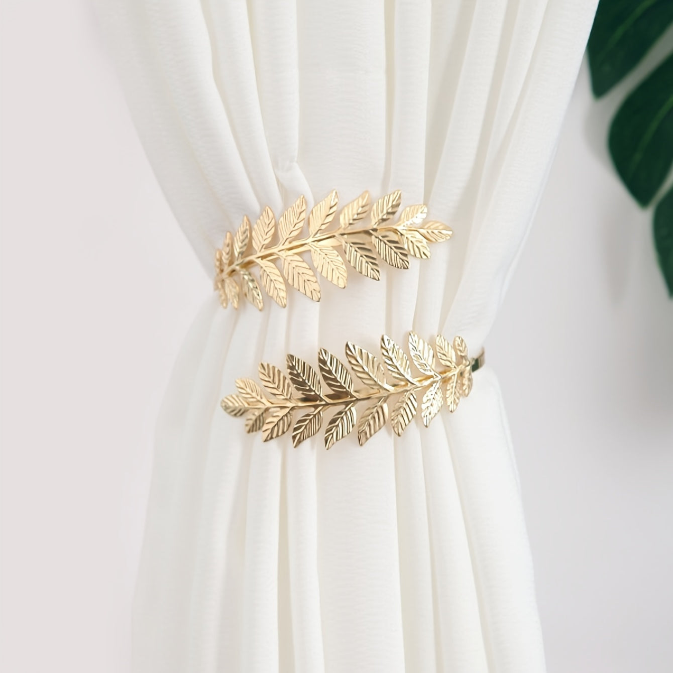 A decorative curtain tieback with gold accents, adorned with branches, leaves, and leaf-shaped hooks, perfect for enhancing home decor.