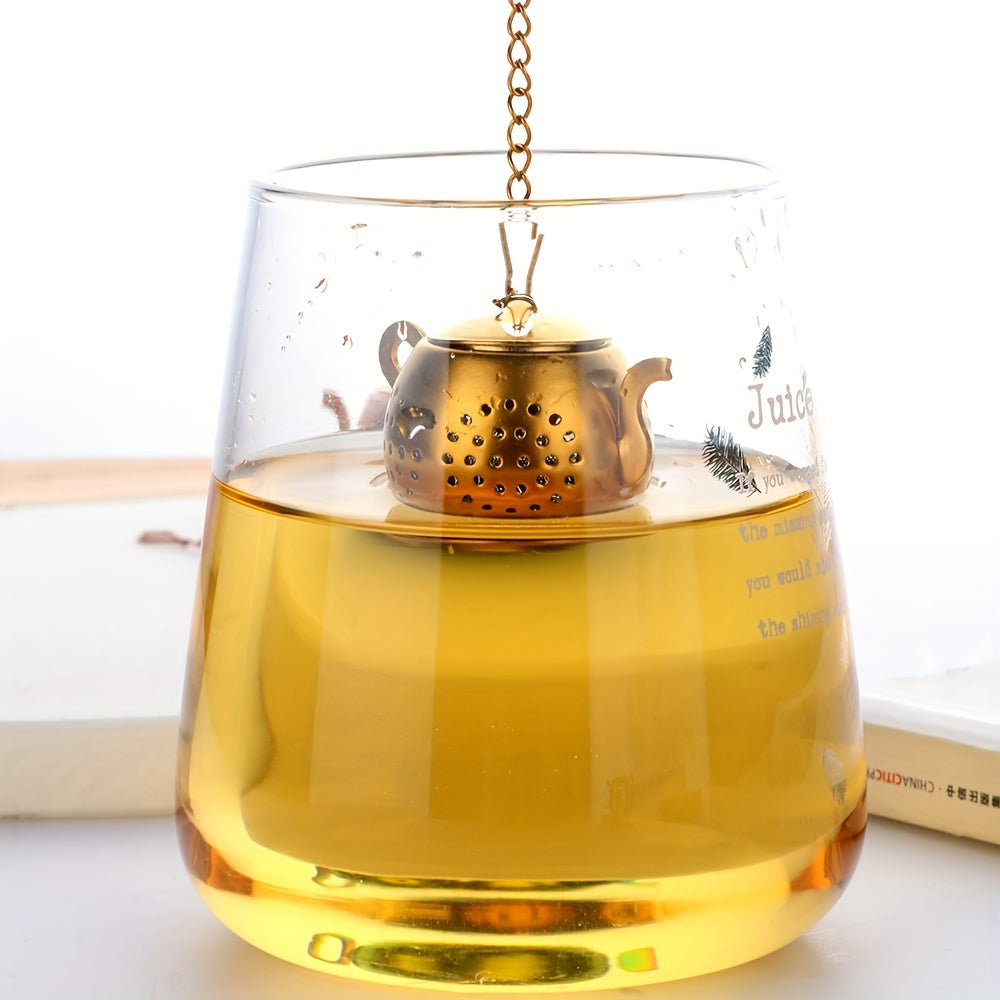 Golden rose stainless steel teapot-shaped tea strainer with uniform filter holes and hanging chain for cups.