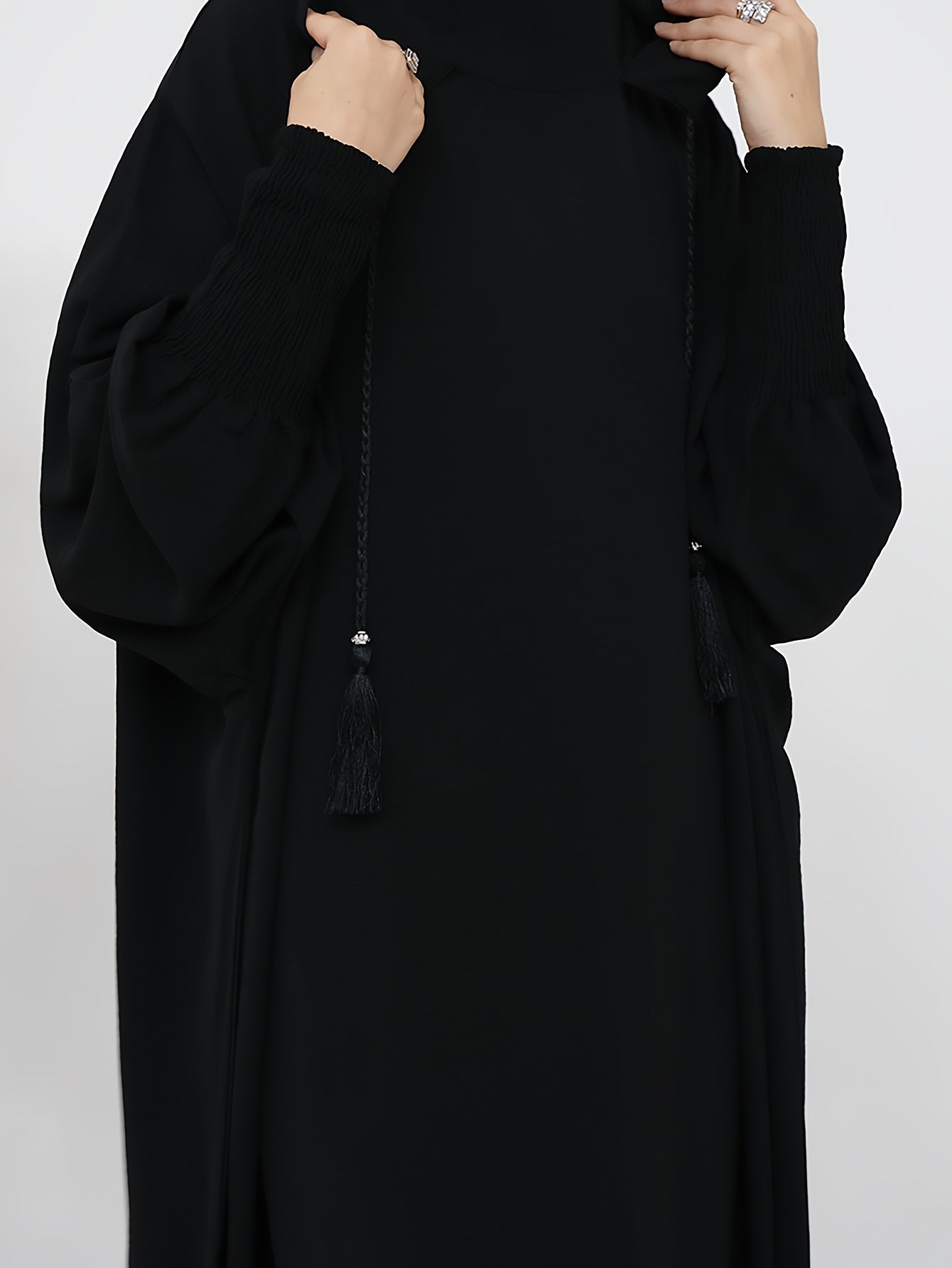 Elegant black abaya with batwing sleeves, drawstring hood, and loose fit. Versatile minimalist style for all seasons. Made of polyester.