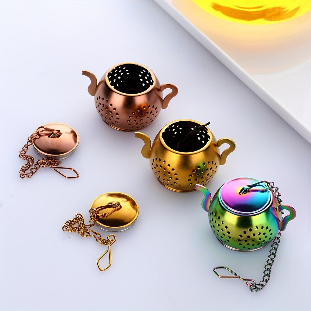 Golden rose stainless steel teapot-shaped tea strainer with uniform filter holes and hanging chain for cups.