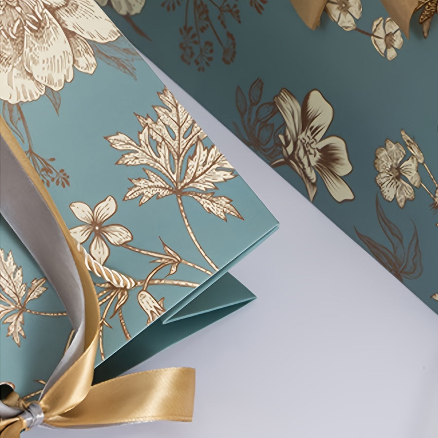 Floral paper gift bag with golden ribbon, teal background, brown, white & gray flowers, suitable for birthdays, weddings, Mother's Day, and special occasions. Features drawstring closure.