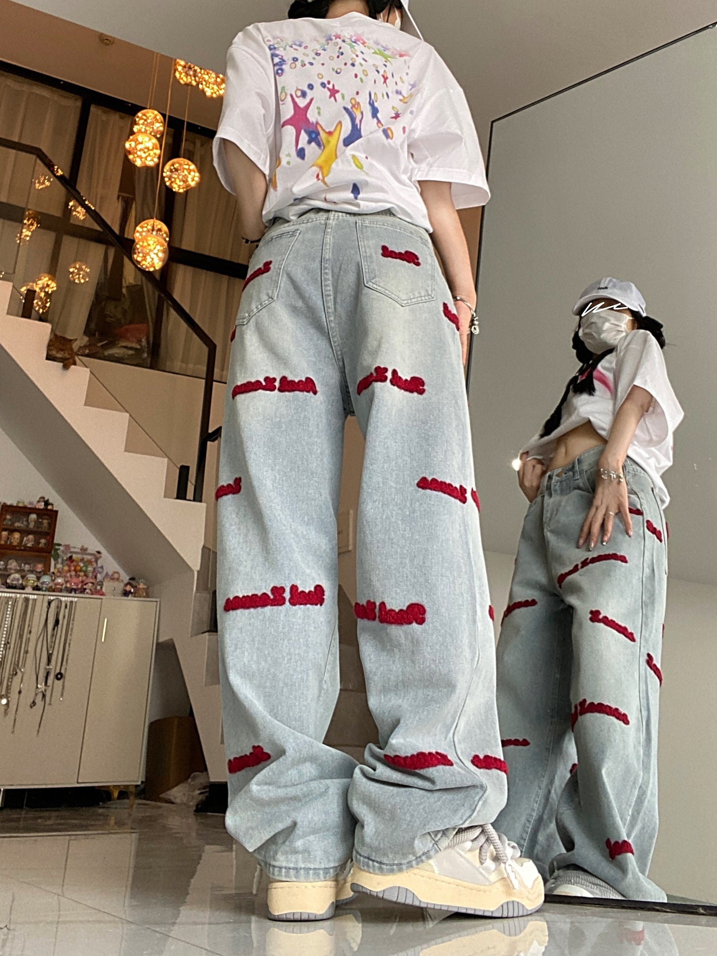 Women's denim jeans with red embroidered lettering, stretch fabric, regular fit, button closure, and washed denim detail. Casual style suitable for all seasons.