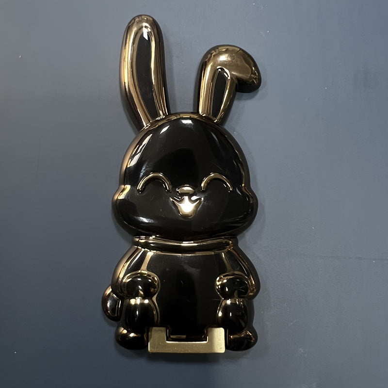 Foldable waterproof phone stand made of ABS material, featuring an adjustable cartoon bunny design for holding smartphones and tablets.