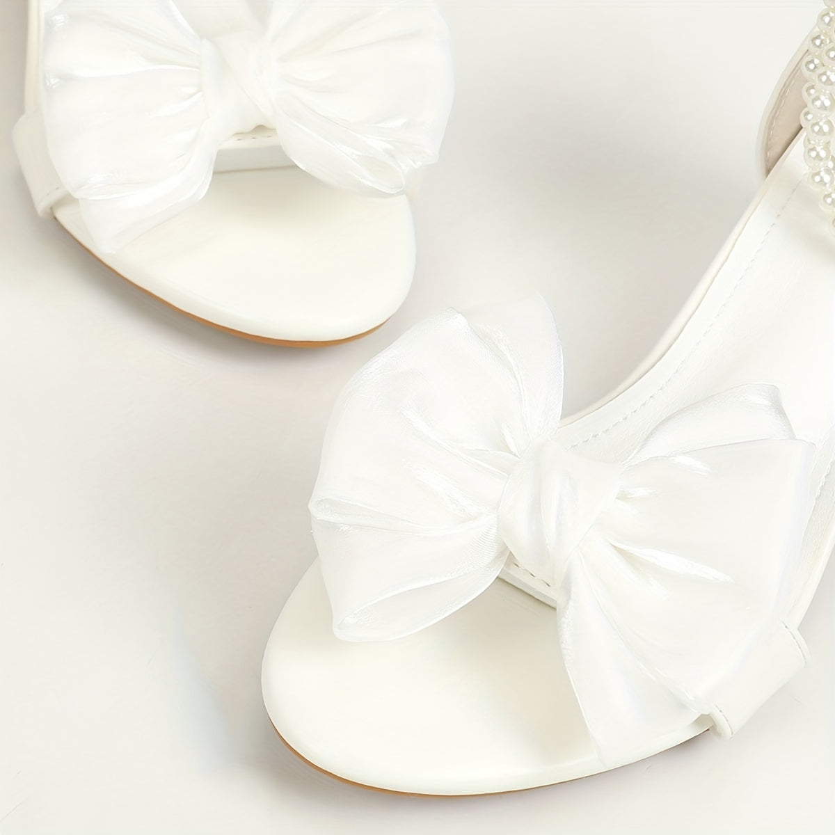 Chunky low heeled sandals with bow decor and faux pearl ankle strap, perfect for evening wear.