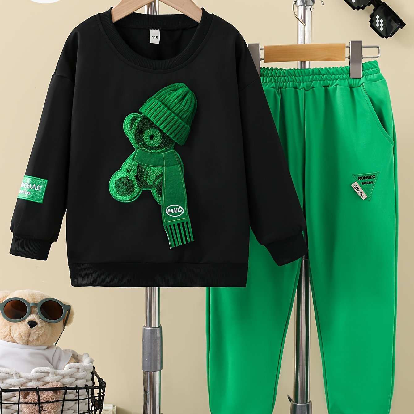 Boys' two-piece suit for outdoor wear with bear print hat, black sweatshirt, and green letter logo trousers.