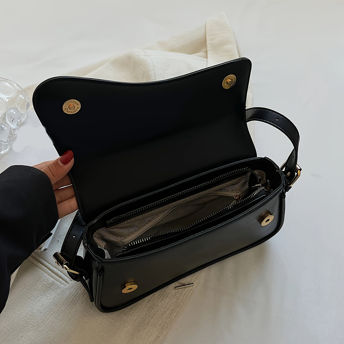 Stylish black baguette bag with adjustable strap, textured flap design, and goldtone hardware. Ideal formal accessory for women.