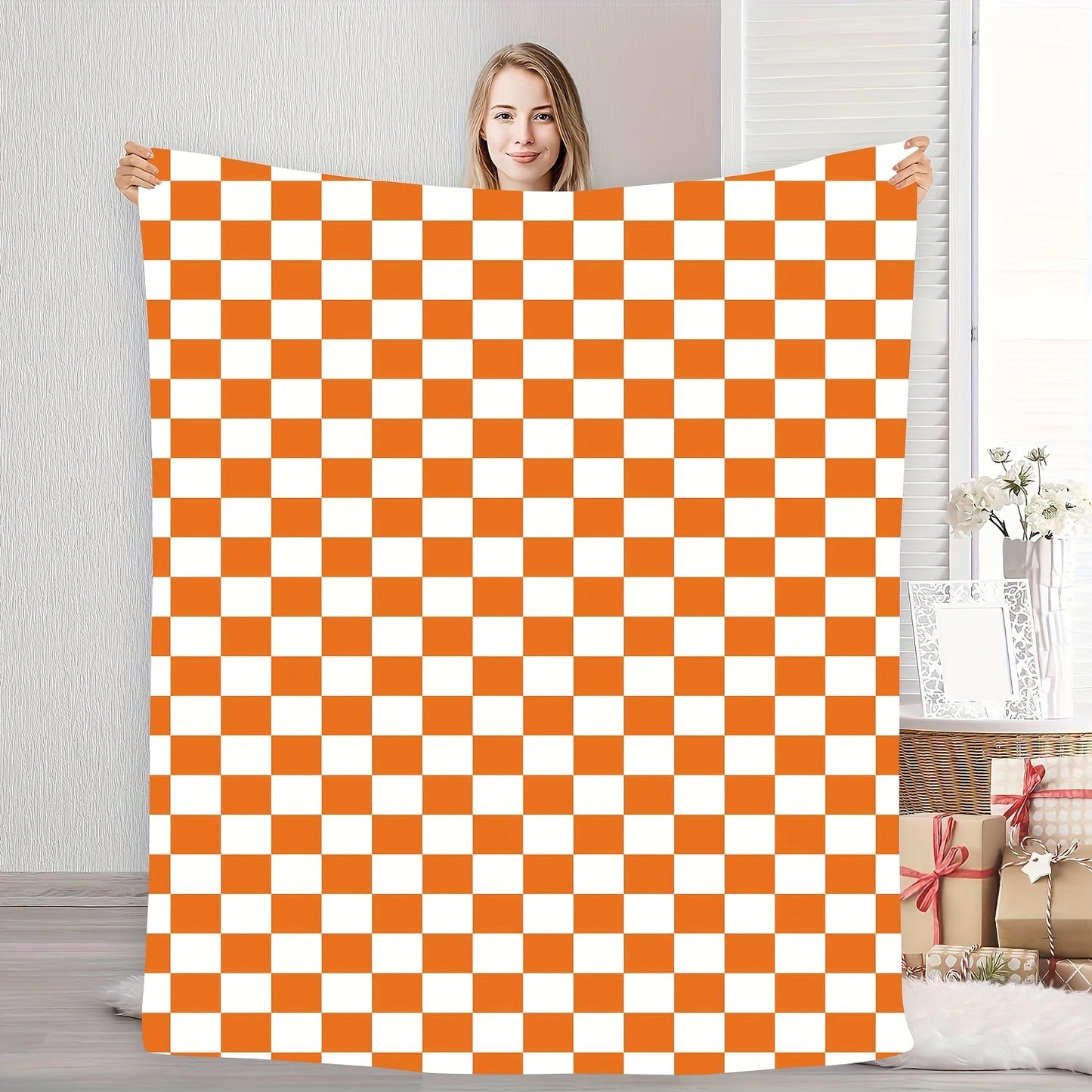 One piece of an orange and white checkered print fleece throw blanket featuring a geometric pattern. This all-season blanket is machine washable, durable, and anti-tear, making it perfect for use in the bedroom, living room, or while camping. It weighs