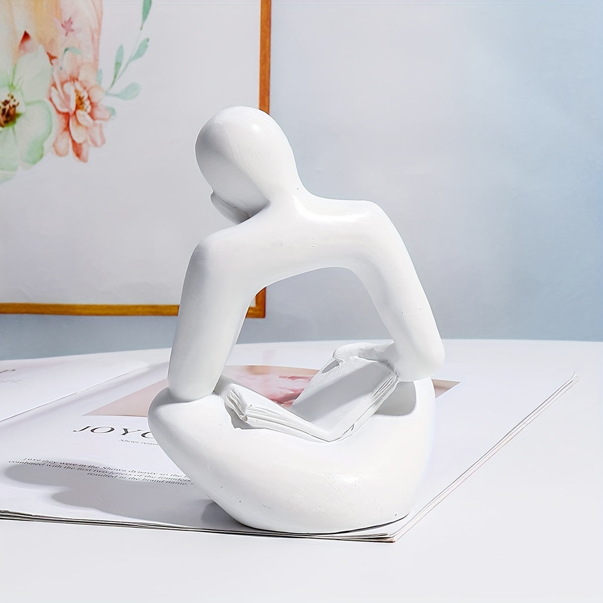 Abstract figure reading book with one hand ornament.