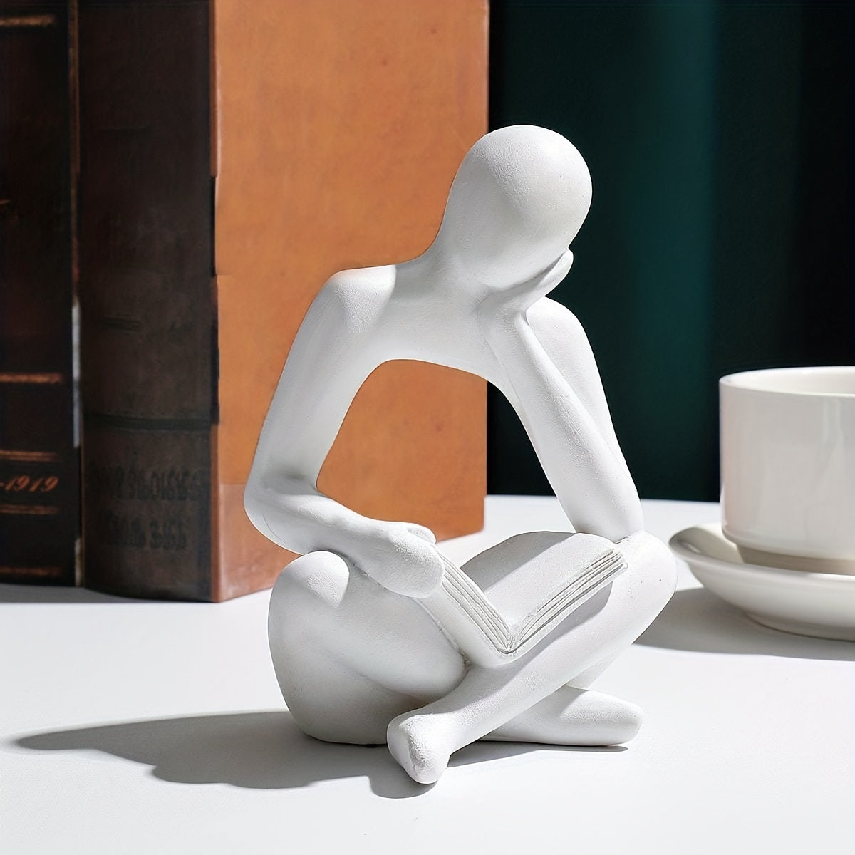 Abstract figure reading book with one hand ornament.