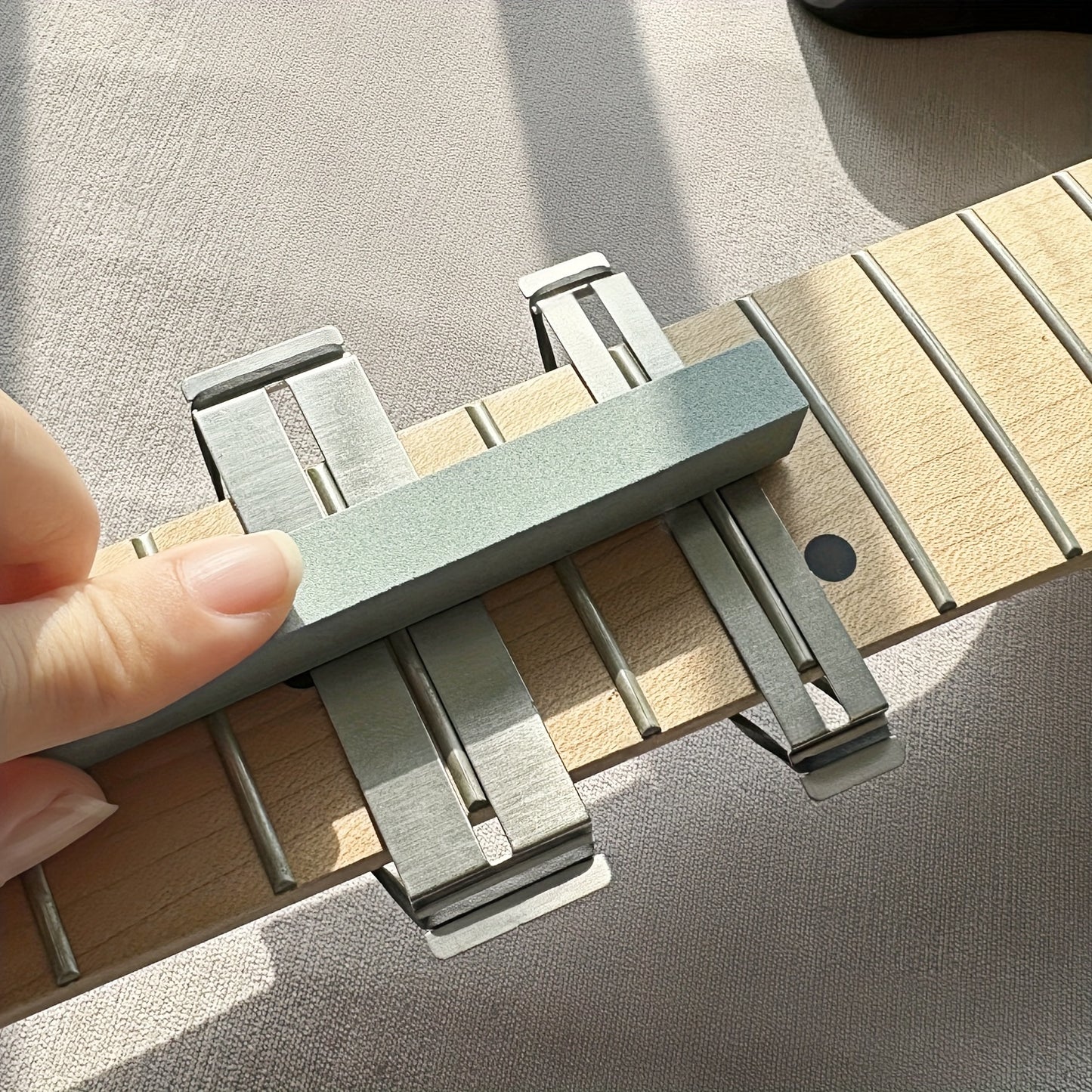 Guitar fretboard maintenance kit with metal protector and grey dressing stones for various string instruments.