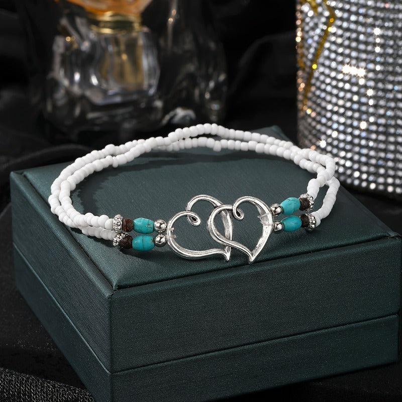 This elegant anklet set features two pieces with double hollowed-out heart shapes adorned with mini seed beads. The design exudes a Bohemian-style charm and is made with stretchy elastic for comfortable wear. A perfect gift for any beautiful woman.