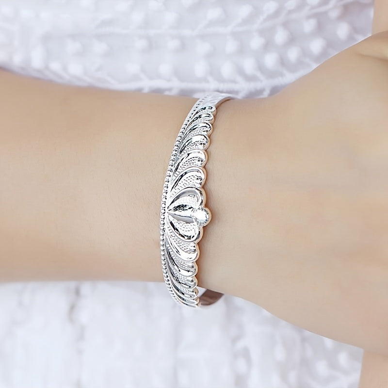 A stunning silver bracelet for women with a crown design, adorned with delicate flowers and shimmering stars. The bracelet features an elegant open mouth clasp for easy wearing.