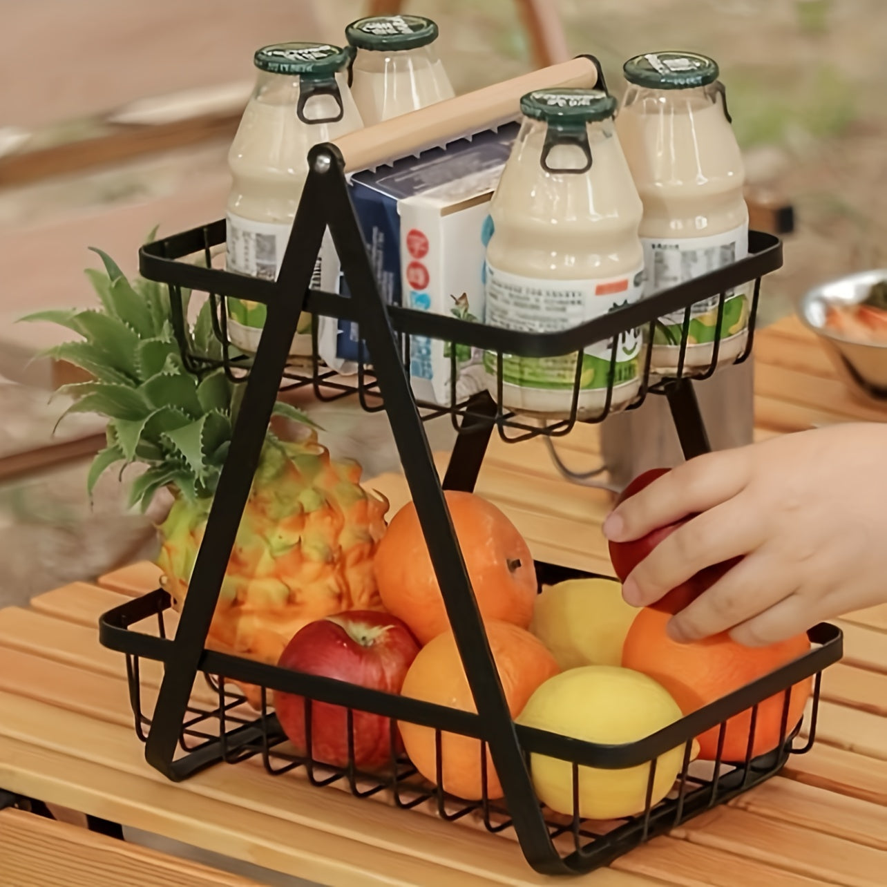 A contemporary metal fruit and vegetable basket featuring a detachable bowl-shaped storage compartment and a wooden handle for kitchen organization. Ideal for gifting during Christmas or Halloween, this handy organizer can be used on the countertop or in