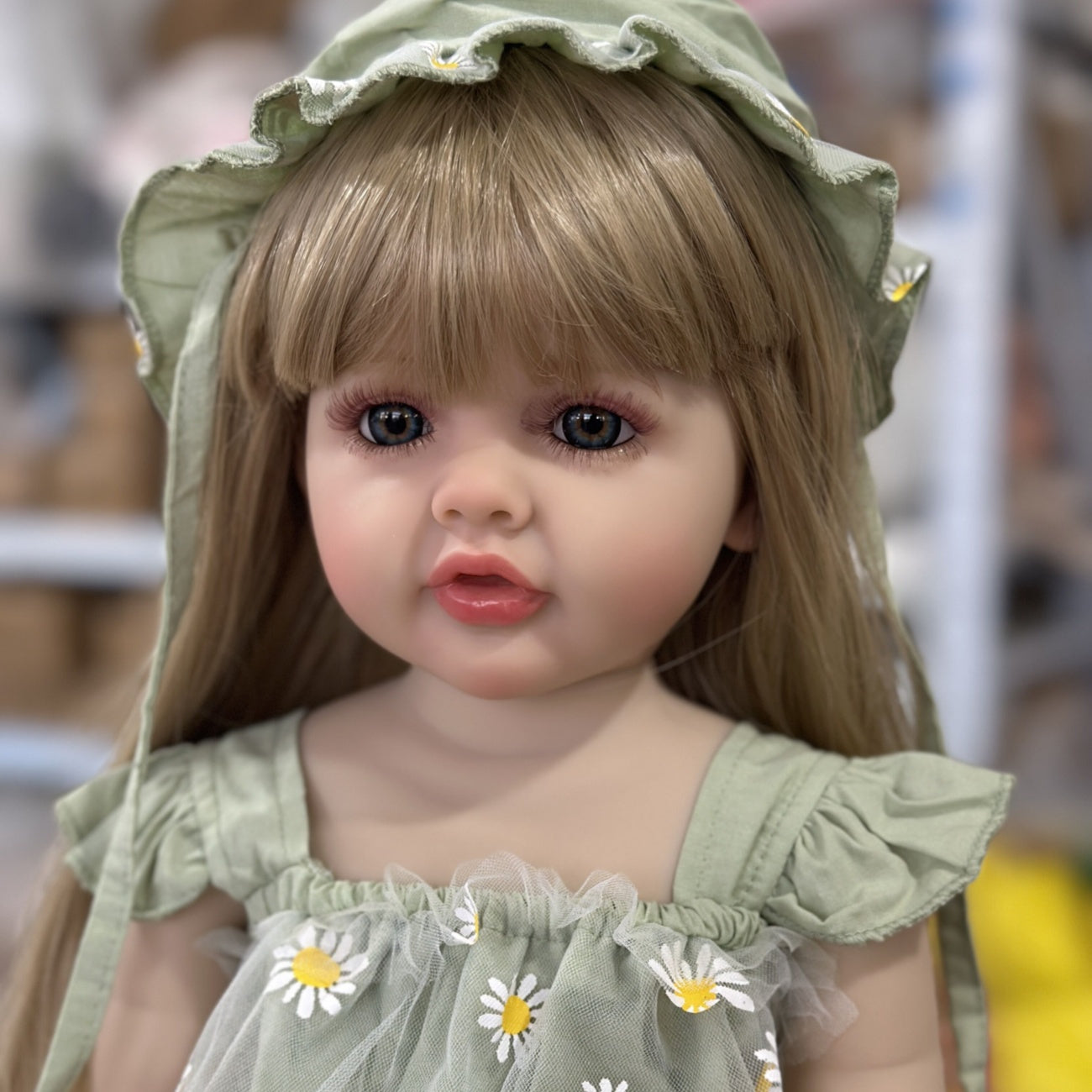 Realistic 55.88 cm full vinyl body reborn baby doll with long blond hair, dressed in a green dress with daisy pattern. Beautiful toddler doll toy for collectors.