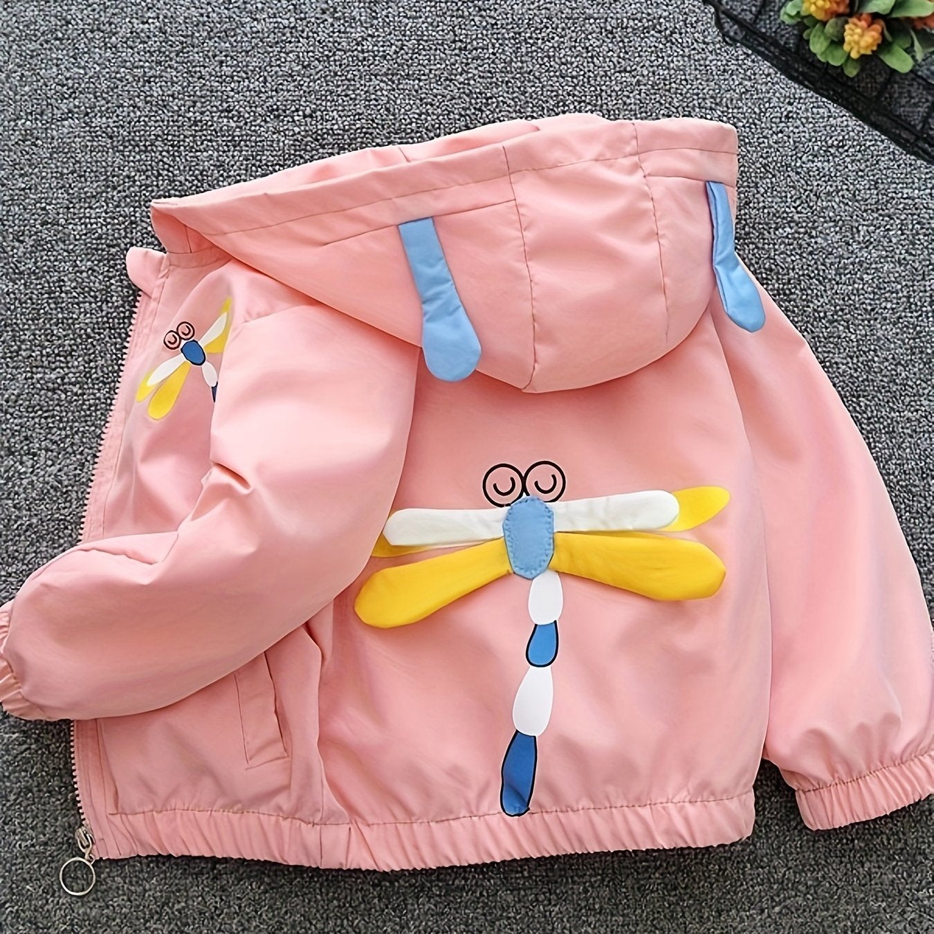 Girls' pink lightweight hooded windbreaker with playful cartoon face design and bow detail. Zip-up style made from polyester blend, perfect for spring and autumn.