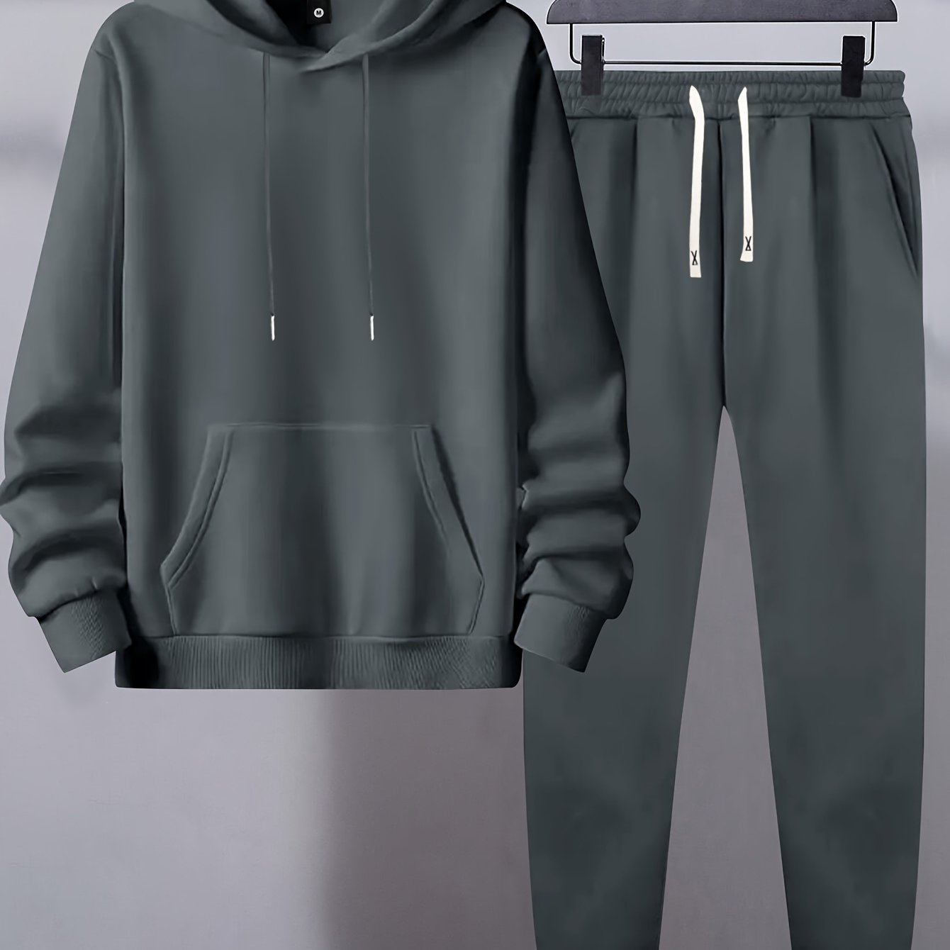 Men's basic polyester sweatsuit set includes a solid color hooded sweatshirt and drawstring joggers with pockets. Made of knit fabric with slight stretch, it has long sleeves and a regular