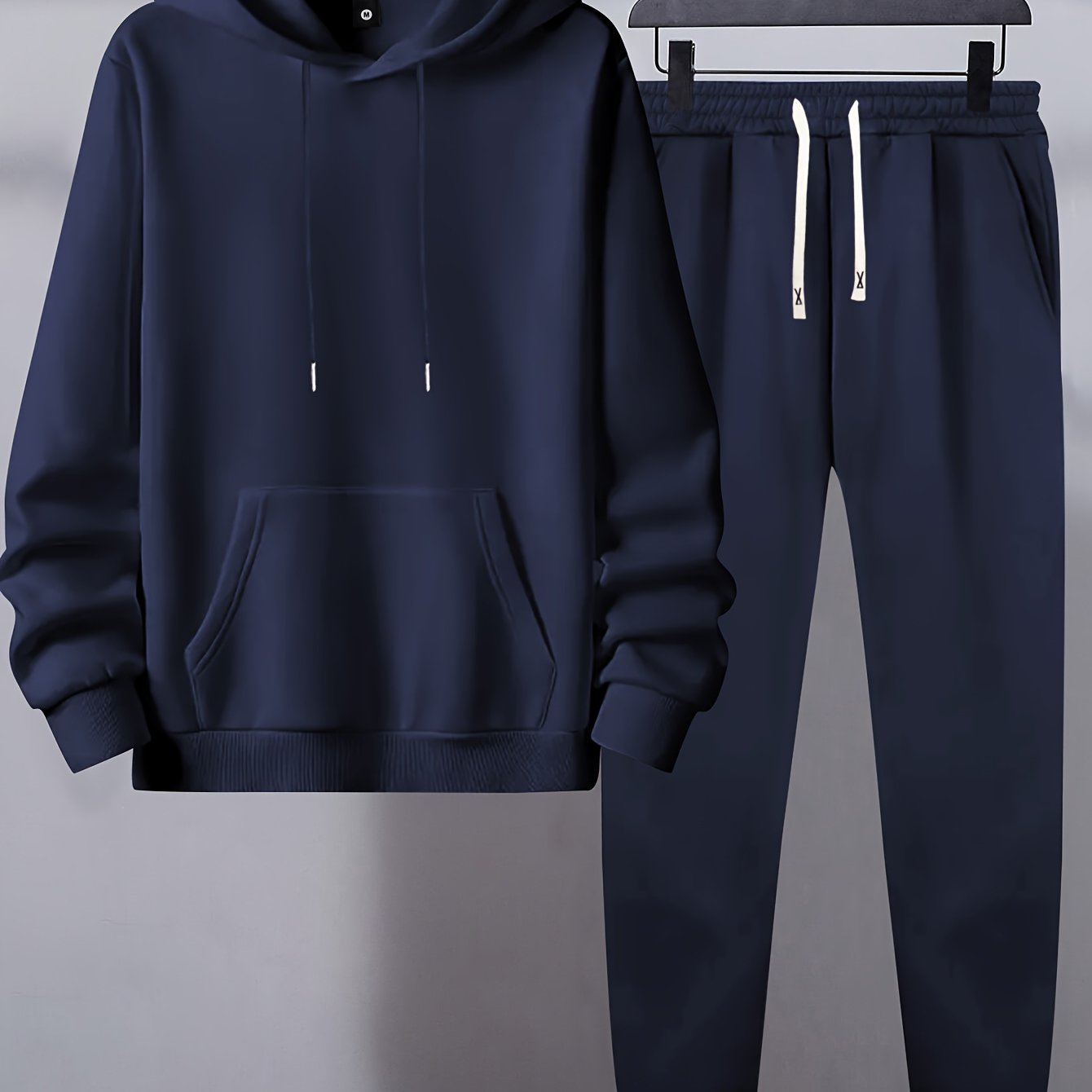 Men's basic polyester sweatsuit set includes a solid color hooded sweatshirt and drawstring joggers with pockets. Made of knit fabric with slight stretch, it has long sleeves and a regular