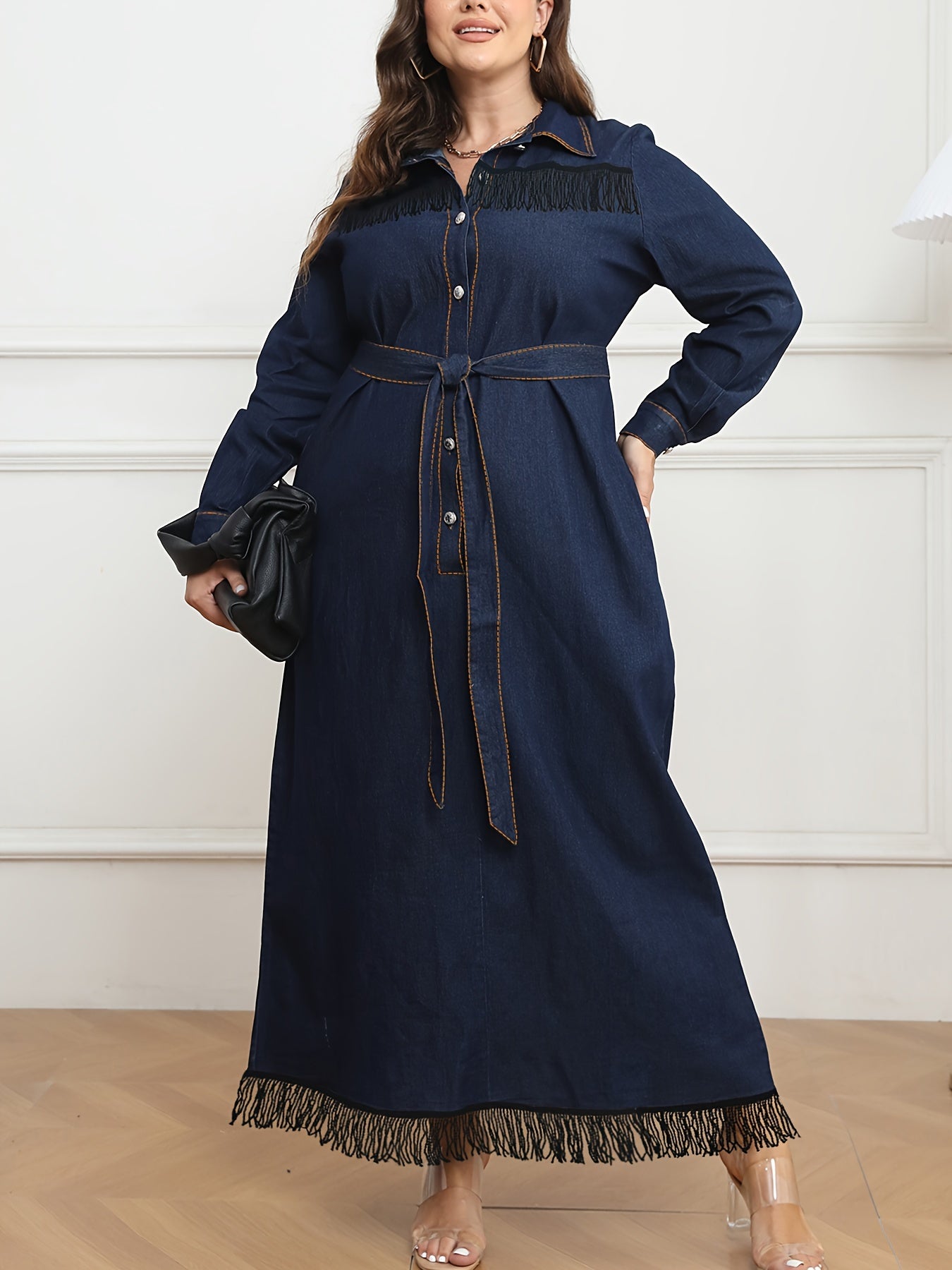 Women's plus size navy blue denim dress with long sleeves, button-up shirt collar, fringe hem, belt detail, and cotton/polyester blend. Machine washable.