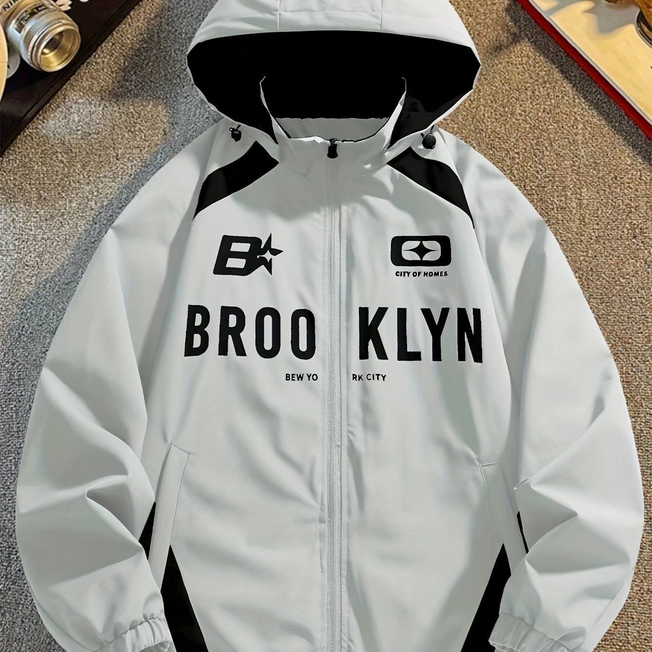 Men's lightweight windproof hooded jacket with Brooklyn-inspired design, side stripe, long sleeves, drawstring detail, and zip-up closure. Made of machine washable polyester.