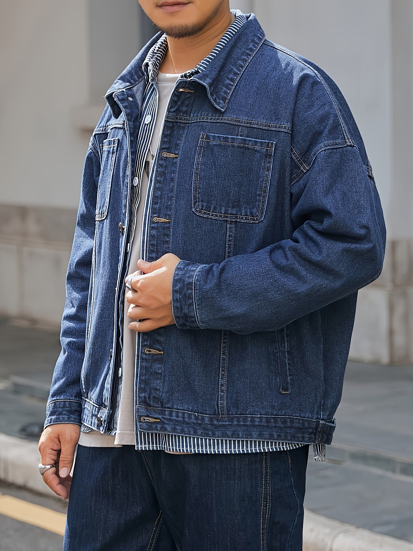 Men's plus size denim jacket in solid washed blue with long sleeves, chest pockets, button-front closure, and loose fit. Machine washable for everyday casual streetwear style with trendy