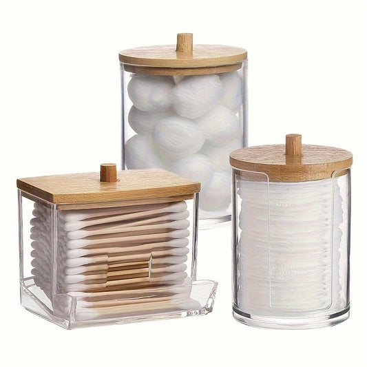 A set of 3 cotton swab holders in clear plastic jars with lids for bathroom organization and storage.