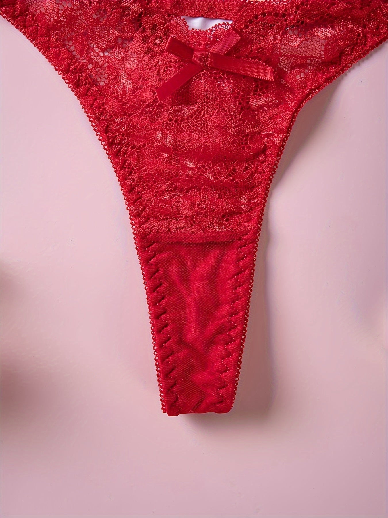 Red lace thong panties with floral print and bow detail, low rise V-shaped design. Made of breathable polyester blend, hand washable. Ideal for intimate moments.