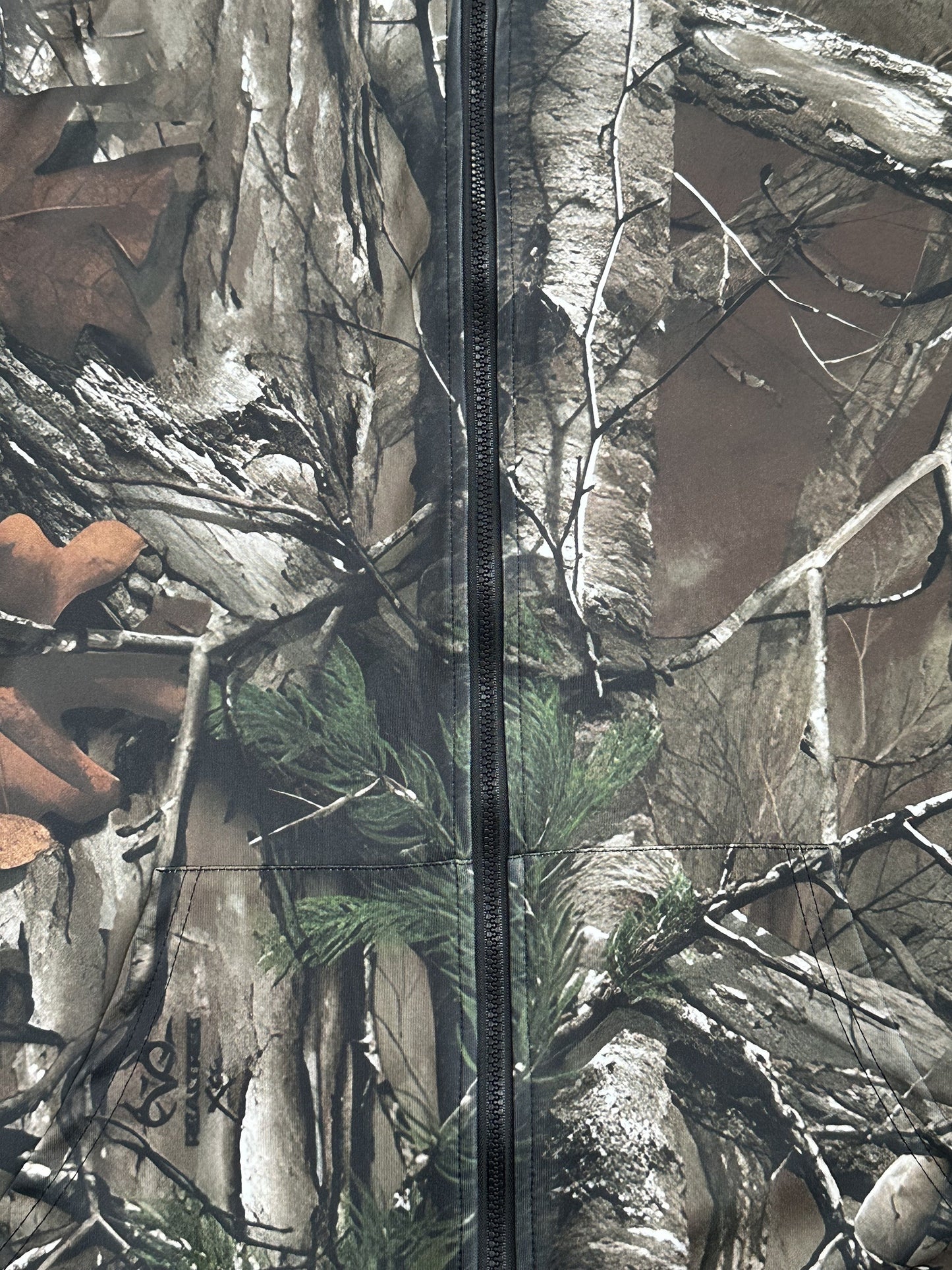 Men's hooded camo jacket in breathable polyester with full-body tree branch print. Features zipper pockets, long sleeves, and a casual outdoor style. Machine washable and available in plus